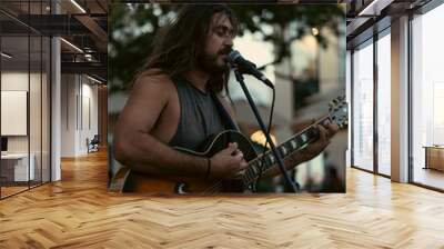 Man musician plays the guitar, sings microphone in the street. Wall mural