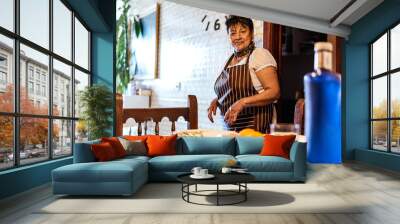 older latin american woman putting things to eat on the table Wall mural