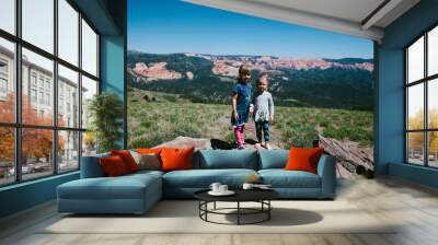 Two little girls hike on red rocks with mountains in summertime Wall mural