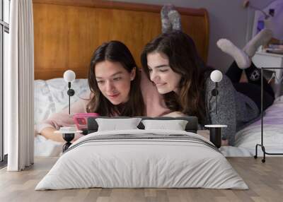 Two young caucasian women lying on bed and looking at cell phone Wall mural