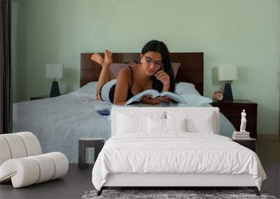 young woman lying in bed reading a book Wall mural