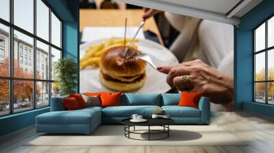 A person is skewering a hamburger. The setting is a cozy restaurant with natural light, perfect for culinary and gastronomic content. Wall mural