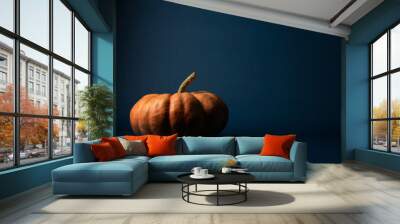 Dark moody blue background with fresh orange seasonal pumpkin for fall or autumn holiday decoration with copy space. Wall mural