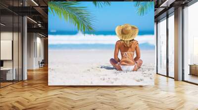 Relax, back view of a woman on the beach and sitting on the sand, Summer vacation or holiday break, freedom or adventure and female person relaxing at the sea with blue sky for peace in nature Wall mural