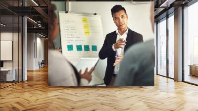 Fielding questions from his team. Shot of a young man giving a presentation to colleagues in an office. Wall mural