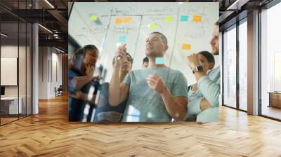 Business people brainstorming, planning and thinking of ideas on a glass board. A group or team of young professional designers using sticky notes to organize their thoughts in a modern office. Wall mural