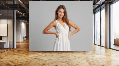 Confident young woman wearing simple white dress posing with hands on hips, smiling brightly. Neutral background, casual fashion style. lifestyle and beauty concepts in marketing and advertising Wall mural