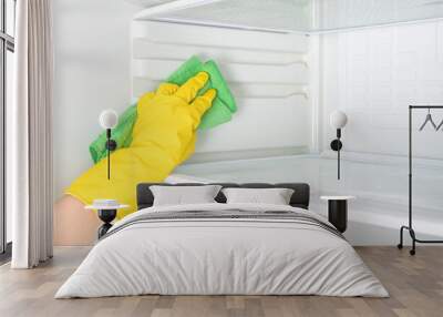 Hand cleaning refrigerator. Person washing refrigerator with rag. Housekeeper wipes shelves of clean refrigerator. Hand in yellow rubber protective glove and green sponge washes. copy space Wall mural