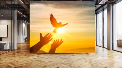 human hands releasing dove of peace into air concept for freedom, peace and spirituality. Silhouette dove flying over human hand at sunset Wall mural