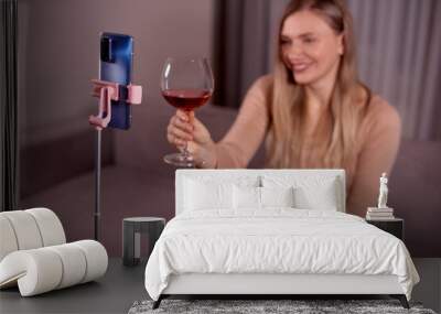 Happy young smiling caucasian woman making video call with smartphone at living room. Best friends drinking red wine and toasting. Video conference party online meeting with family. Stay home. Wall mural