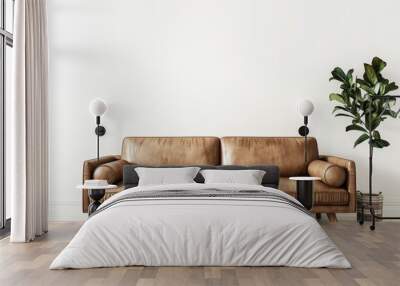 A brown leather sofa with wooden legs and a large plant sits in front of a white wall Wall mural