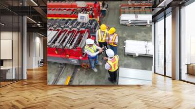 Senior engineer manager trains new employees within the metal sheet factory. Everyone wear safety vest and hardhat. Large machines and metal sheets are in the working area. Wall mural