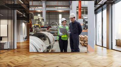 Two people are working in a factory. They are discussing plans while looking at a laptop. They wear safety helmets. Wall mural