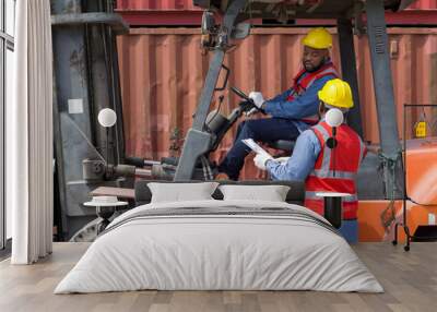 Two short black hair man with moustache and beard dressed in hardhat, safety vest and protective glove working during the day under sunlight. There are container in the work area. Wall mural