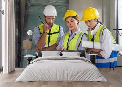 Young architect pointing at laptop computer monitor explain to foreman and engineer about a floor plan. Everyone wear helmet and safety vest. Work environment at construction site of housing project. Wall mural