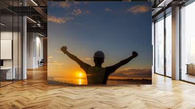 Concept of success and freedom with a young engineer holding his arms up in the sunset. engineer working on building site. Wall mural