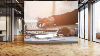 A businessman analyzing investment charts at workplace and using laptop and touch tablet. Wall mural