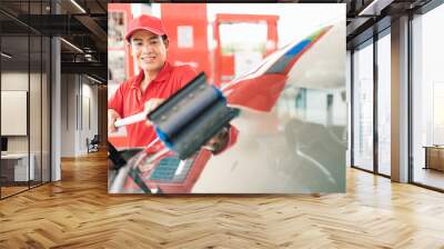 Asian gas station worker man cleaning windshield while car owner waiting for filling energy power fuel in car tank into petrol station, commercial service for benzine, diesel, gasohol, gasoline Wall mural