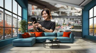 Happy asian woman looking at her phone in the city Wall mural