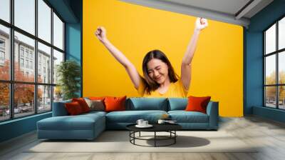 Happy woman make winning gesture isolated over yellow background Wall mural