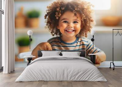  A cheerful child with curly hair, smiling and eating a plate of pasta with vegetables. Wall mural