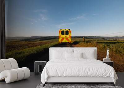 Ambulance car of emergency medical service leaving on rural dirt road in the middle of fields. Themes urgency, rescue and health care in remote location.. Wall mural