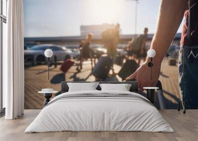 Group of people walking to airport terminal at summer sunset. Selective focus on hand of man with suitcase. . Wall mural