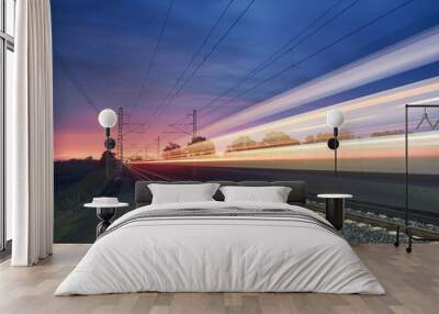 Modern railway at beautiful sunrise. Light trail of high speed train on railroad track. Moving modern intercity passenger train.. Wall mural