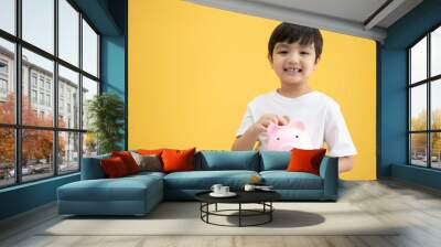 Piggy bank and little Asian boy with coin on yellow background. Smiling happy with good habit for future education. Insurance concept pre schooler Wall mural