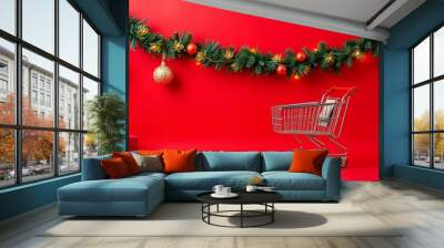 Shopping cart filled with various Christmas decorations including ornaments, lights, and garland on a festive red background, shopping, holiday, red background Wall mural