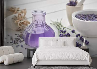 Dry lavender flowers, bottle of essential oil or flavored water, sachet and mortar on white wooden table. Wall mural