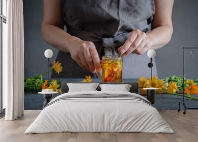 Woman making healthy tea with calendula or marigold flowers. Wall mural