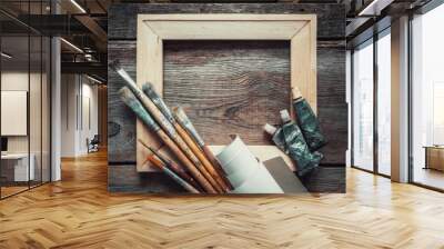 Wooden stretcher bar, paintbrushes, roll of artist canvas and paint tubes on old wooden background. Top view. Copy space for text. Wall mural