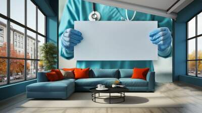 Medical professional holding a blank sign, wearing scrubs and blue gloves. Wall mural