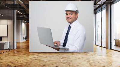 Asian civil engineer operate with laptop to control working in studio. Worker wearing hard hat using laptop computer standing on isolated white background.. Wall mural