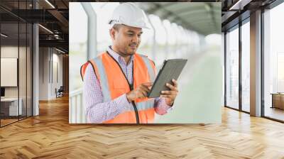 Asian civil engineer operate with tablet to control working at construction. Worker wearing hard hat at highway concrete road site. Wall mural