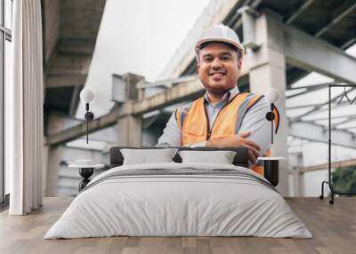 Asian engineer handsome man or architect looking construction with white safety helmet in construction site. Standing at highway concrete road site. Wall mural