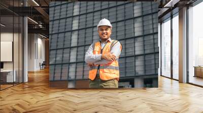 Asian engineer handsome man or architect looking forward with white safety helmet in construction site. Standing at modern building construction. Worker asian man working project building Wall mural