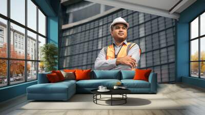 Asian engineer handsome man or architect looking forward with white safety helmet in construction site. Standing at modern building construction. Worker asian man working project building Wall mural