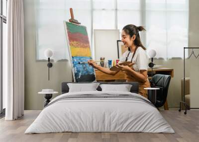 Asian woman artist working on painting with brush and variant acrylic color. Female artist painter on canvas in creative studio as art concept Wall mural