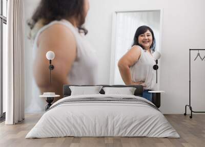 Body positive plus size female clothing. Body positive plus size woman happily and is proud of herself looking at mirror at home. Try wearing clothes that measure the size. Wall mural