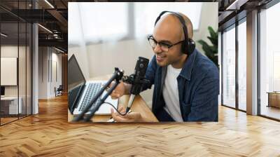 Content creator asia man host streaming his a podcast on laptop with headphones and condenser microphone interview guest conversation at home broadcast studio. Male blogger recording voice over radio Wall mural