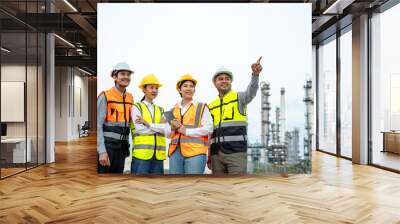 Group of Asian engineer people with safety helmet standing front of oil refinery. Industry zone gas petrochemical. Factory oil storage tank and pipeline. Workers team work in refinery construction Wall mural