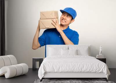 Happy delivery asian man in blue uniform standing holding box parcel cardboard on isolated white background. Smiling male service worker. Delivery courier and shipping service. Wall mural