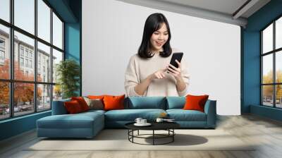 Pretty young asian woman using smartphone standing on isolated w Wall mural