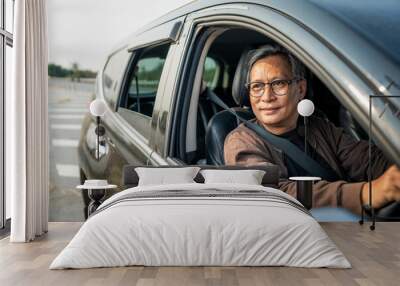 Senior Asian man drives a car vehicle on a clear day. With beautiful blue sky. He smiling driving to travel by car. Old man getting new car. Wall mural