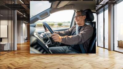 Senior Asian man drives a car vehicle on a clear day. With beautiful blue sky. He smiling driving to travel by car. Old man getting new car. Wall mural