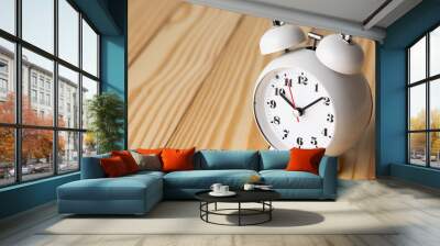 Small white alarm clock, black numbers, set the time for 10.10 o'clock, placed on a wood table. Wall mural