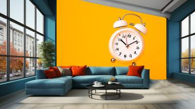 Small white alarm clock, black numbers, set the time placed on a table. Clock on isolated yellow background. Wall mural