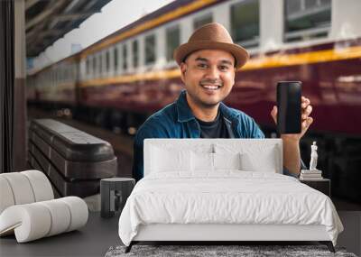 Traveler young asian man using cellphone booking trip at terminal train station. Happy tourist travel by train using smartphone searching location. Male Backpacker arrival at platform railway. Wall mural